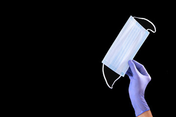 A hand in a blue medical glove holds a medical mask. Protection against viruses and bacteria. Protection against COVID-19. Medicine and healthcare concept. Copy space.