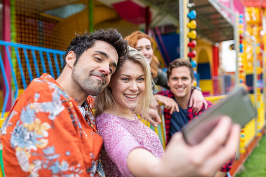 Smiling woman taking selfie with friends through smart phone at amusement park