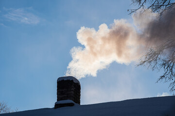 Smoky house chimney on a cold, sunny, snowy winter morning