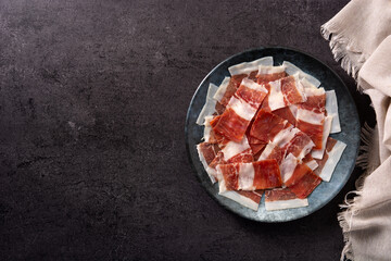 Spanish serrano ham slices on black plate on black background. Top view. Copy space