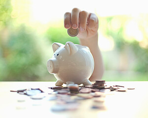 Boy inserting coin in piggy bank on table