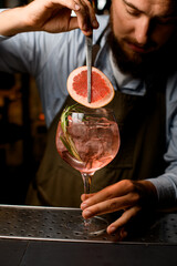 view of goblet glass with cold cocktail that the hand of barman decorating by a slice of grapefruit using tweezers