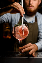 Front view of goblet glass with cold cocktail that the hand of barman decorating by a slice of grapefruit using tweezers