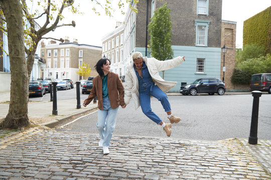 Mid adult woman jumping by girlfriend walking on footpath