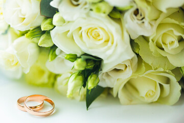 Golden wedding rings and wedding bouquet of pale yellow roses