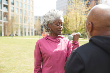 Senior woman exercising with man in public park