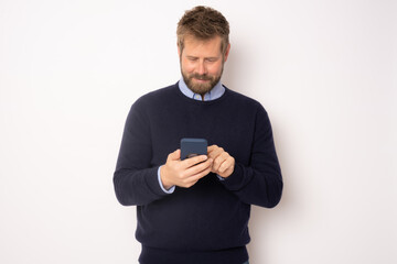 Young smiling handsome man using smartphone standing isolated over white background.