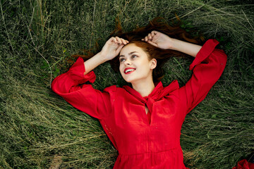 cheerful woman in a red dress lies on the grass top view