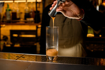 Fototapeta na wymiar hand of bartender skilfully poured syrup into tall transparent glass on the bar