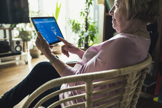 Senior woman checking smart home device while sitting on chair