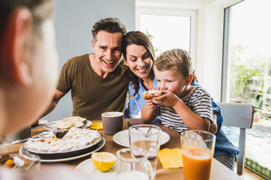 Man with woman looking at son eating pie during breakfast
