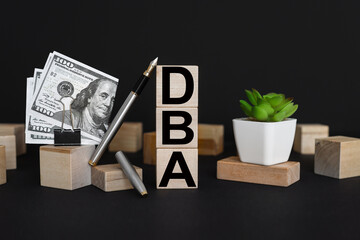 DBA. Side view of three empty wooden cubes isolated on a black background. Place for your text. business concept. pen and money