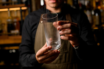hands of a male bartender gently hold empty transparent tall cocktail glass.