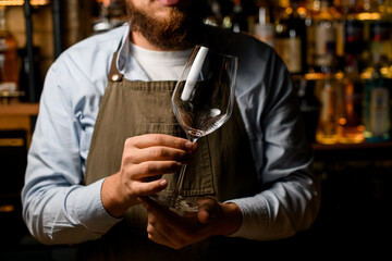 close-up of male bartender hands gently holding an empty wine goblet glass.