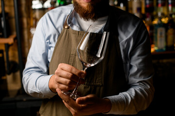 hands of a male bartender gently hold empty transparent wine goblet glass.