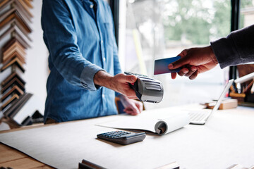 Male frame maker holding credit card reader while customer paying in workshop