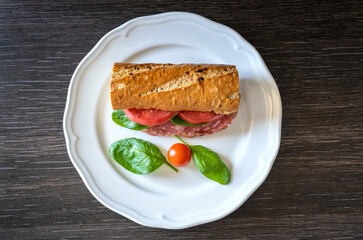 Sandwich with  salami, mozzarella and tomatoes on a white plate, closeup. Italian style cuisine.