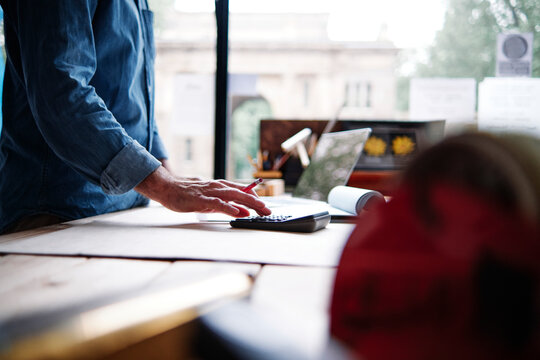 Male store owner using calculator while making financial bill in workshop