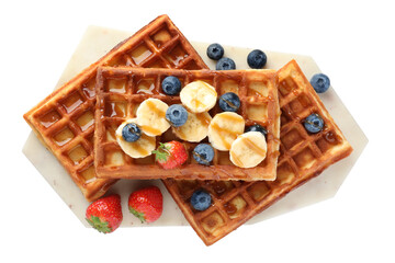 Board with delicious Belgian waffles, banana, berries and caramel sauce isolated on white, top view