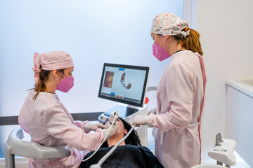 Female dentist wearing protective face masks doing surgery of patient's teeth in clinic