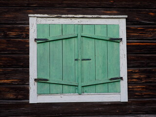 Obraz na płótnie Canvas Window with closed wooden shutters, old scandinavian white window with green shutters on brown wall, Öjebyn, Sweden