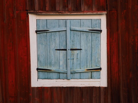 Window with closed wooden shutters, old scandinavian white window with blue shutters on warm brown wall, Öjebyn, Sweden