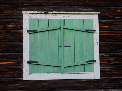 Window with closed wooden shutters, old scandinavian white window with green shutters on brown wall, Öjebyn, Sweden