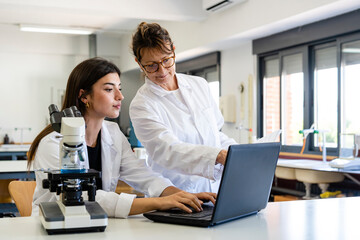 Mature female scientist and young colleague discussing over laptop at laboratory
