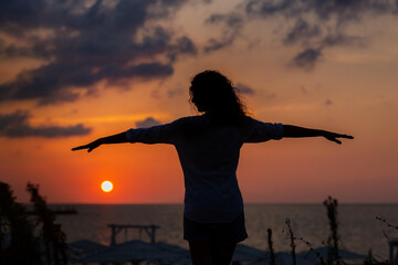 Happy young woman having fun with open hands at the sunset on sea.