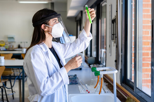 Young female scientist wearing protective face mask examining chemical at laboratory