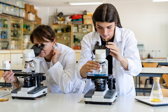 Female scientists examining chemical through microscopes at laboratory