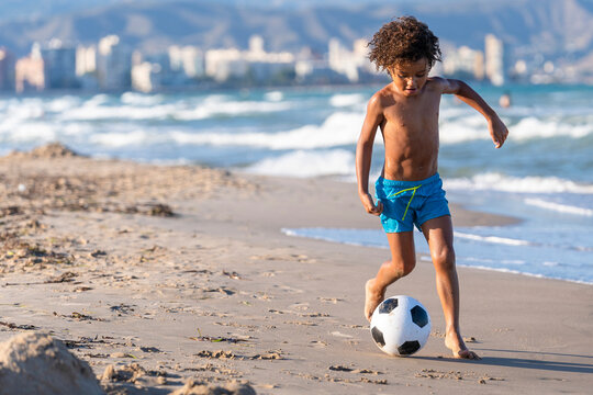 Shirtless boy playing with soccer ball at beach