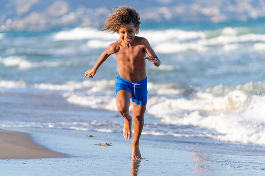 Cheerful boy running on coastline at beach