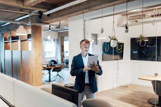 Senior male entrepreneur using digital tablet while standing in office