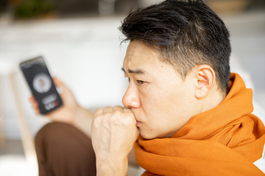 Sick asian man having video call with his doctor on smartphone. Concept of online medicine and health care. Idea of medical mobile app. Blurred image of male person with scarf on neck at home