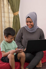 an Asian hijab mother is working from home using a laptop