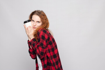 a young girl in a plaid shirt holds a cup of coffee on a light background