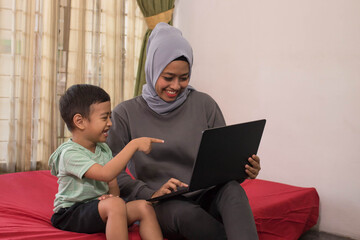 an Asian hijab mother is working from home using a laptop