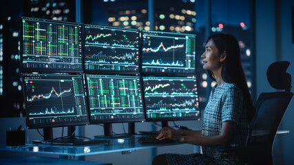 Financial Analyst Working on a Computer with Multi-Monitor Workstation with Real-Time Stocks, Commodities and Exchange Market Charts. Businesswoman at Work in Investment Broker Agency Office at Night.