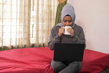 Asian women in hijab are drinking tea and working from home