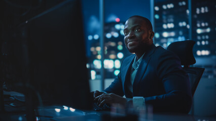 Financial Analyst Working on Computer with Multi-Monitor Workstation with Real-Time Stocks, Commodities and Exchange Market Charts. African American Trader Works in Investment Bank Late at Night.