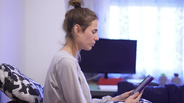 Young beautiful caucasian woman sitting on bed at home with e-book reader