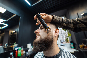 Barber works with a beard clipper. Hipster client getting haircut. - obrazy, fototapety, plakaty