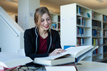 Young woman studying in a library smiling and enjoying reading her study books
