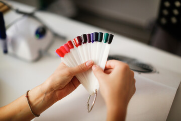 Beauty saloon. Cute Caucasian girl young woman in pink gloves makes manicure client with long hair....