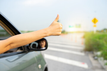 Hand of woman traveler showing thumbs up from through window on the road go to enjoy trip. Lady driving her car on holiday vacation time. The symbol of a hand raised for help when the car is broken.