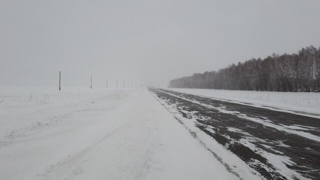 Steadicam pan from empty siberian intercity highway to snowed field when strong wind and heavy snowstorm in evening. Power line is on the field