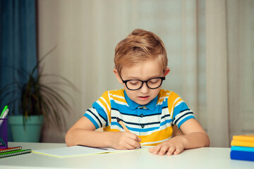 Naklejka premium School child with glasses is doing homework sitting at the table at home.