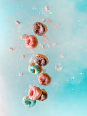 assortment of donuts with sprinkles flying out from a pink cup in a cloud of sugar and marshmallows on bright blue background. Birthday or party celebration food. levitation trend concept. High