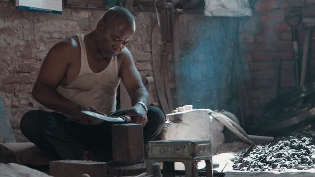 Medium shot blacksmith sharpening knife on anvil in workshop